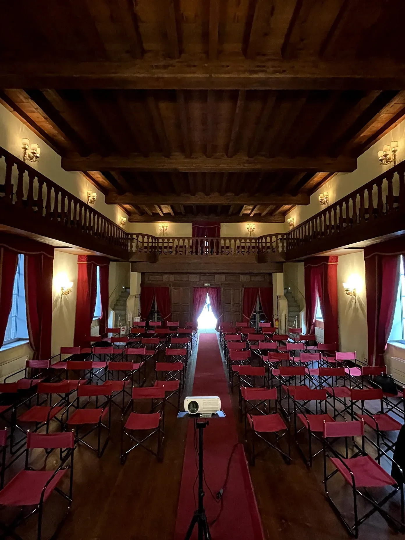 A small historic theater prepared for an Intré company camp, with red chairs, a projector, wooden balconies, and warm wall lights.